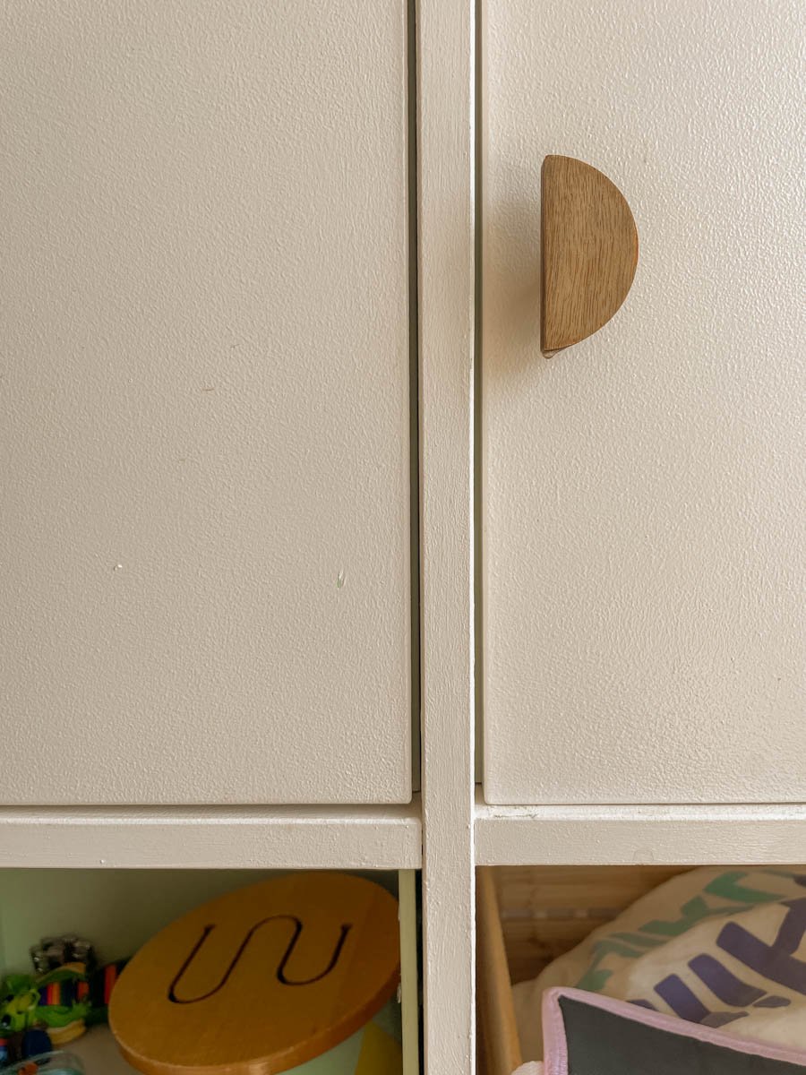 A close-up of a light-colored cabinet with wooden half-moon handles.
