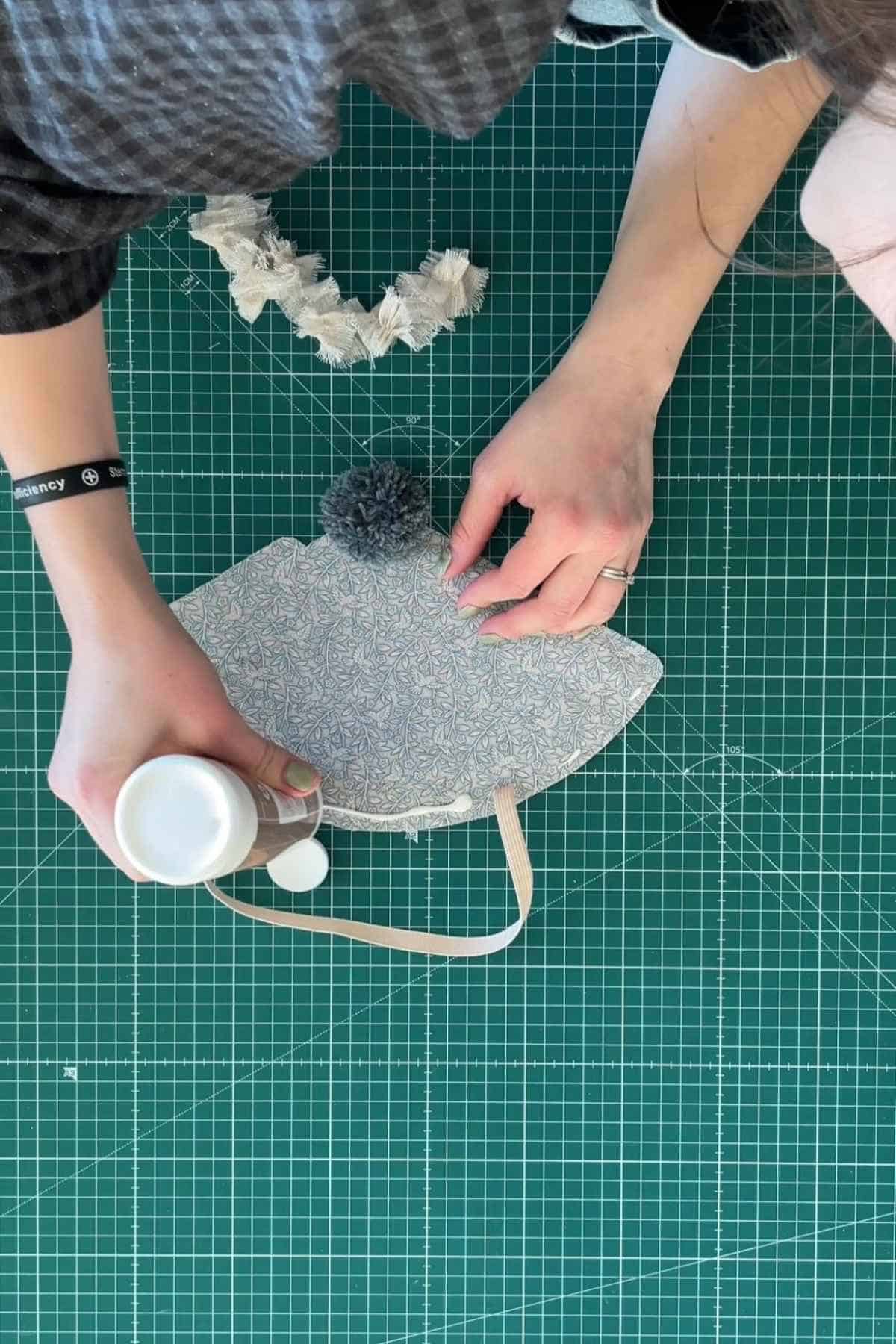 A person applies glue to the bottom of a party hat. The decorative trim for the hat lies above.