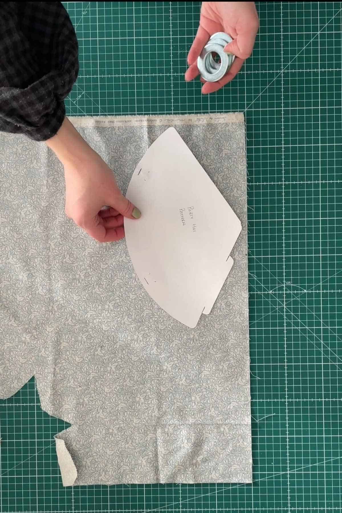 Person placing a free template for a DIY party hat onto floral fabric on a green cutting mat, while holding white measuring tape.