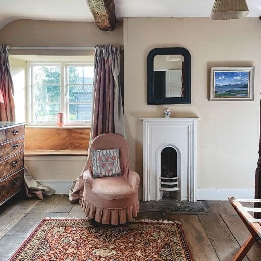 A cosy cottage living room with small antique fireplace and pink antique chair