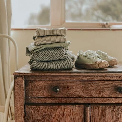 A pile of sustainable kids clothes from the brand Kidly, sitting on top of an antique cabinet