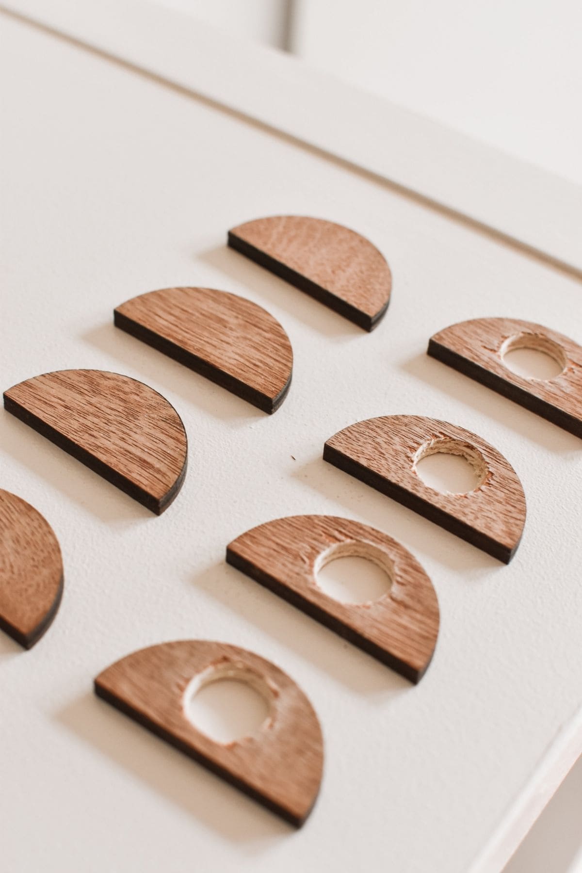 Wooden semicircles with small circular cutouts are neatly arranged on a white surface. The pieces, displayed in two rows, showcase their smooth finish and natural wood grain.