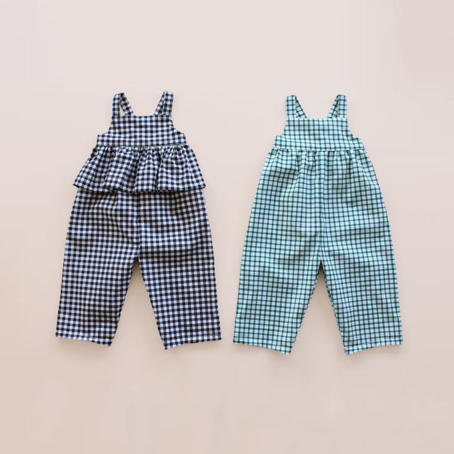 Two children’s jumpsuits laid flat side by side on a beige background, one with black and white gingham and a ruffled top, the other blue and green gingham with a straight top—perfect inspiration for childrens sewing patterns.