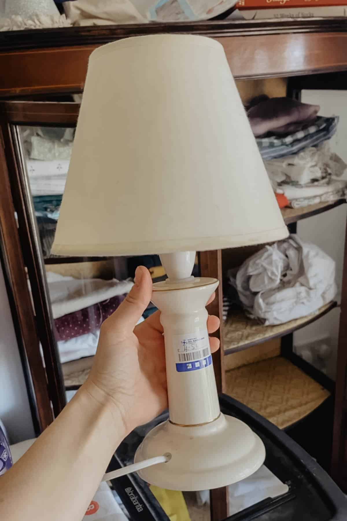A person holding a thrifted vintage lamp in front of a cabinet.