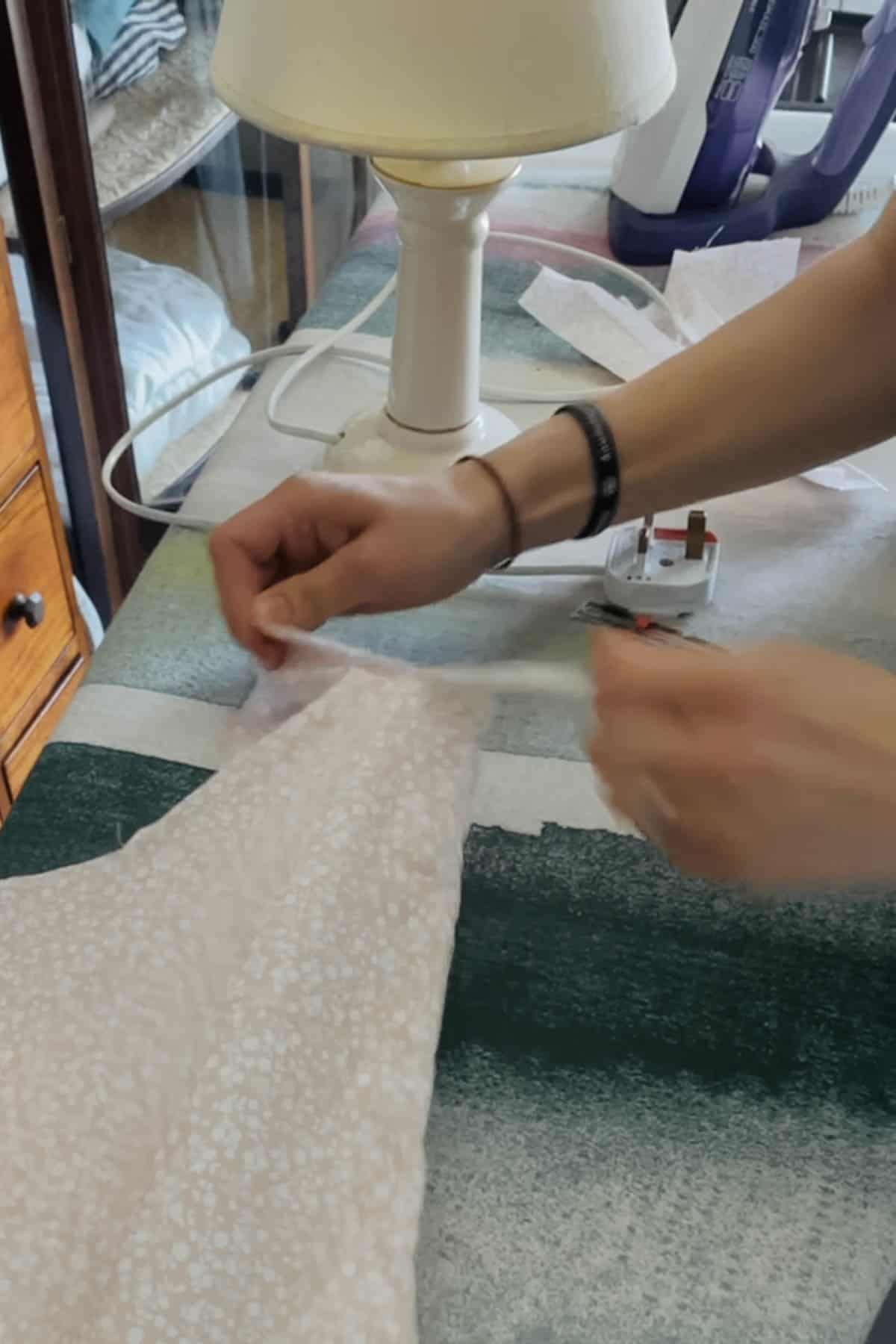 A person tears a piece of pink floral fabric.
