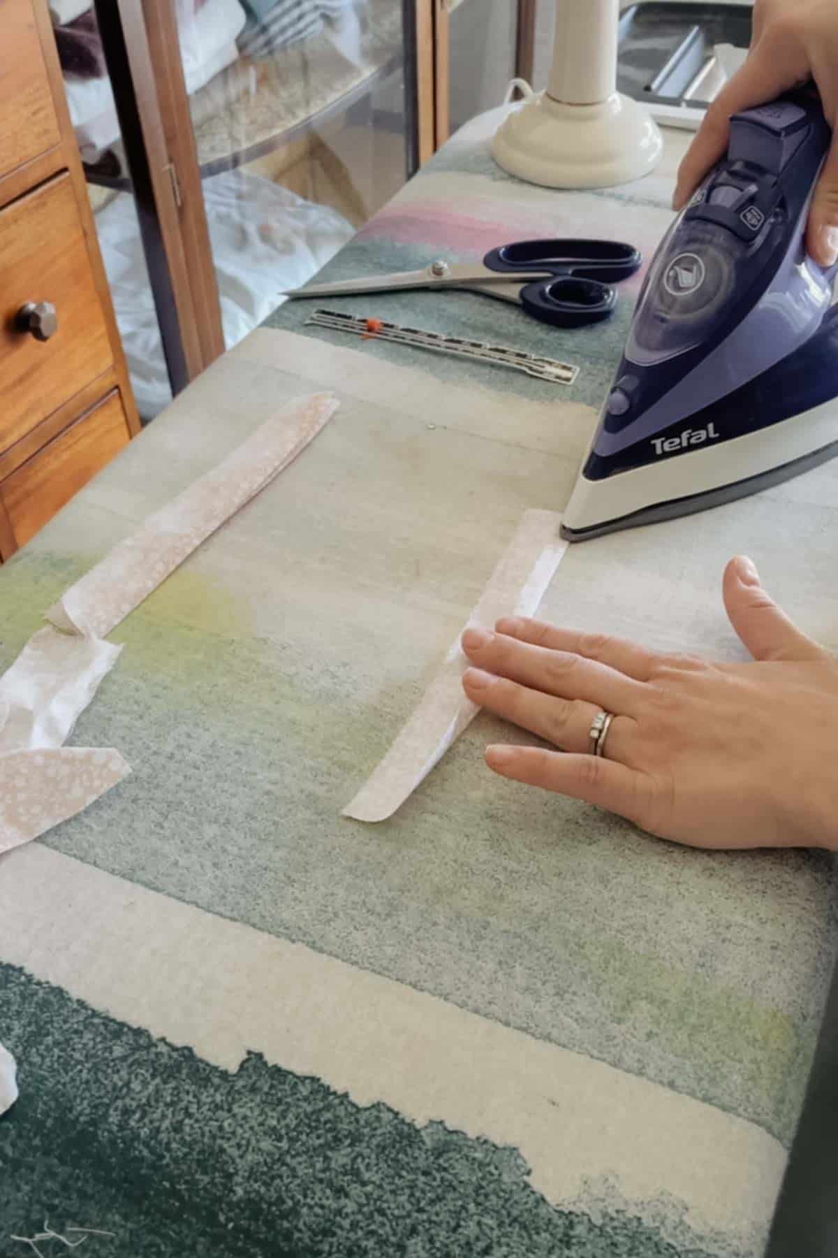 A person irons the folded edge of a piece of pink floral fabric