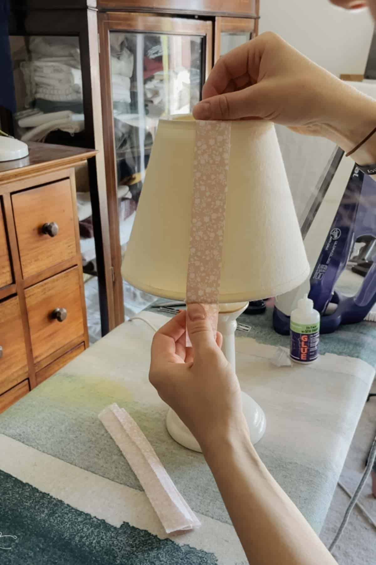 A person places a strip of floral fabric onto a lampshade
