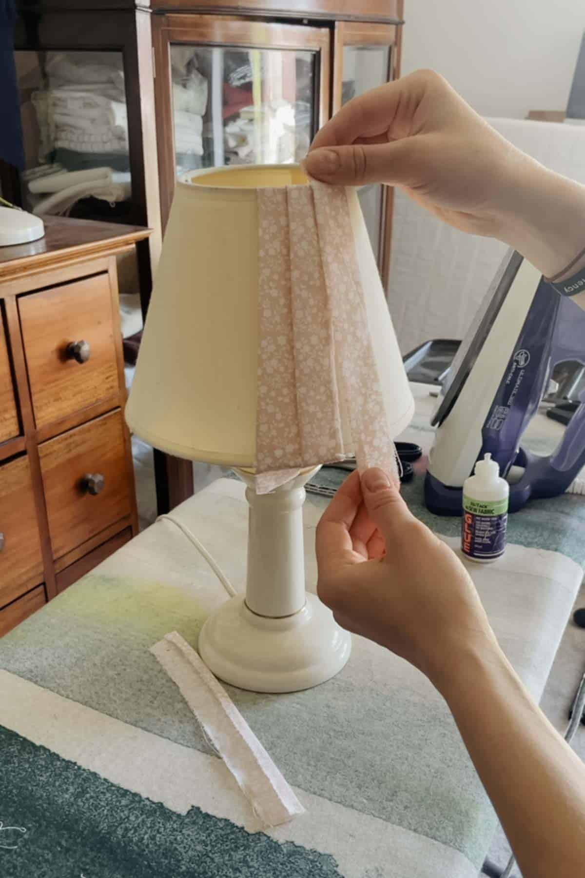 A person places a strip of floral fabric onto a lampshade