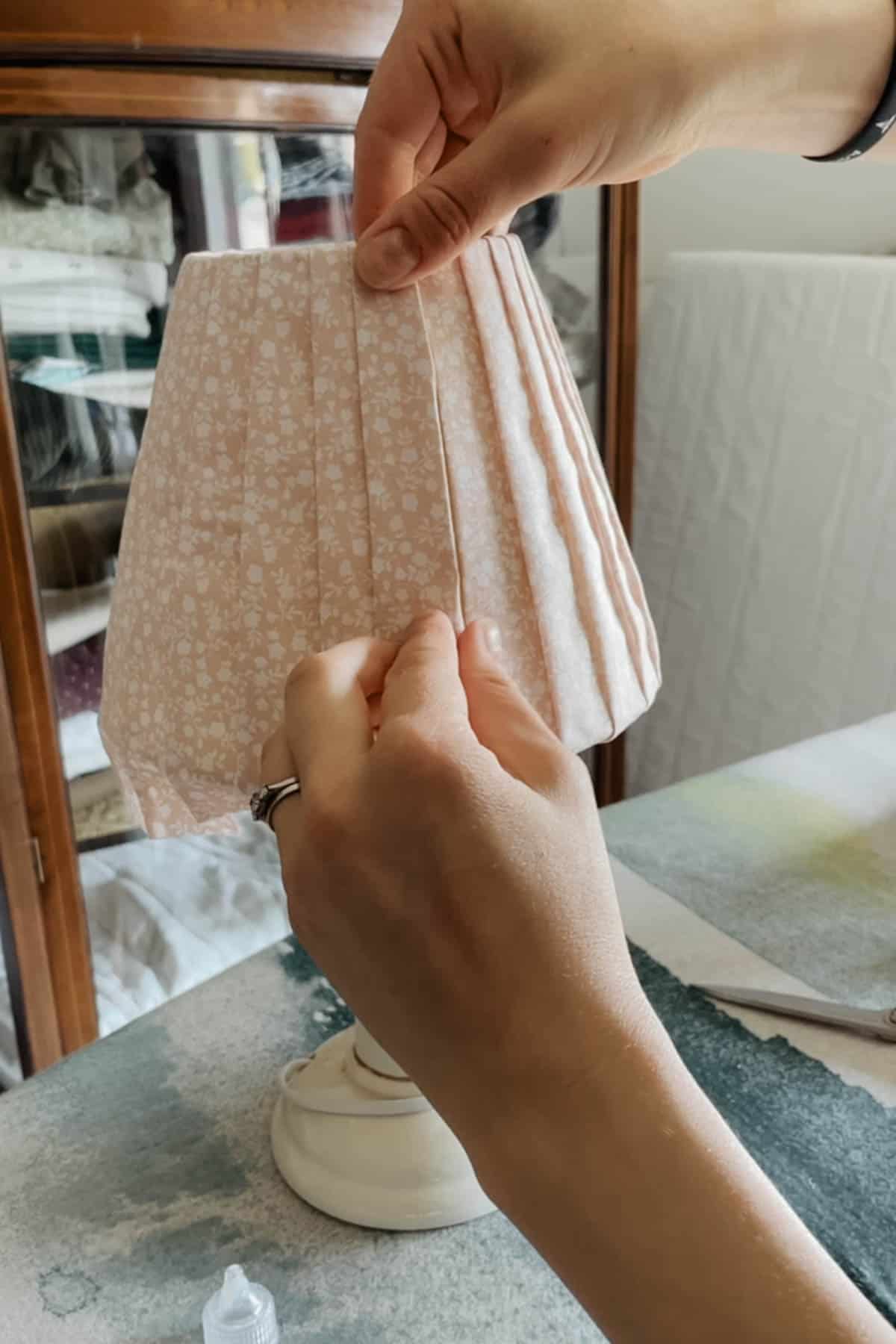 A person places a strip of floral fabric onto a lampshade