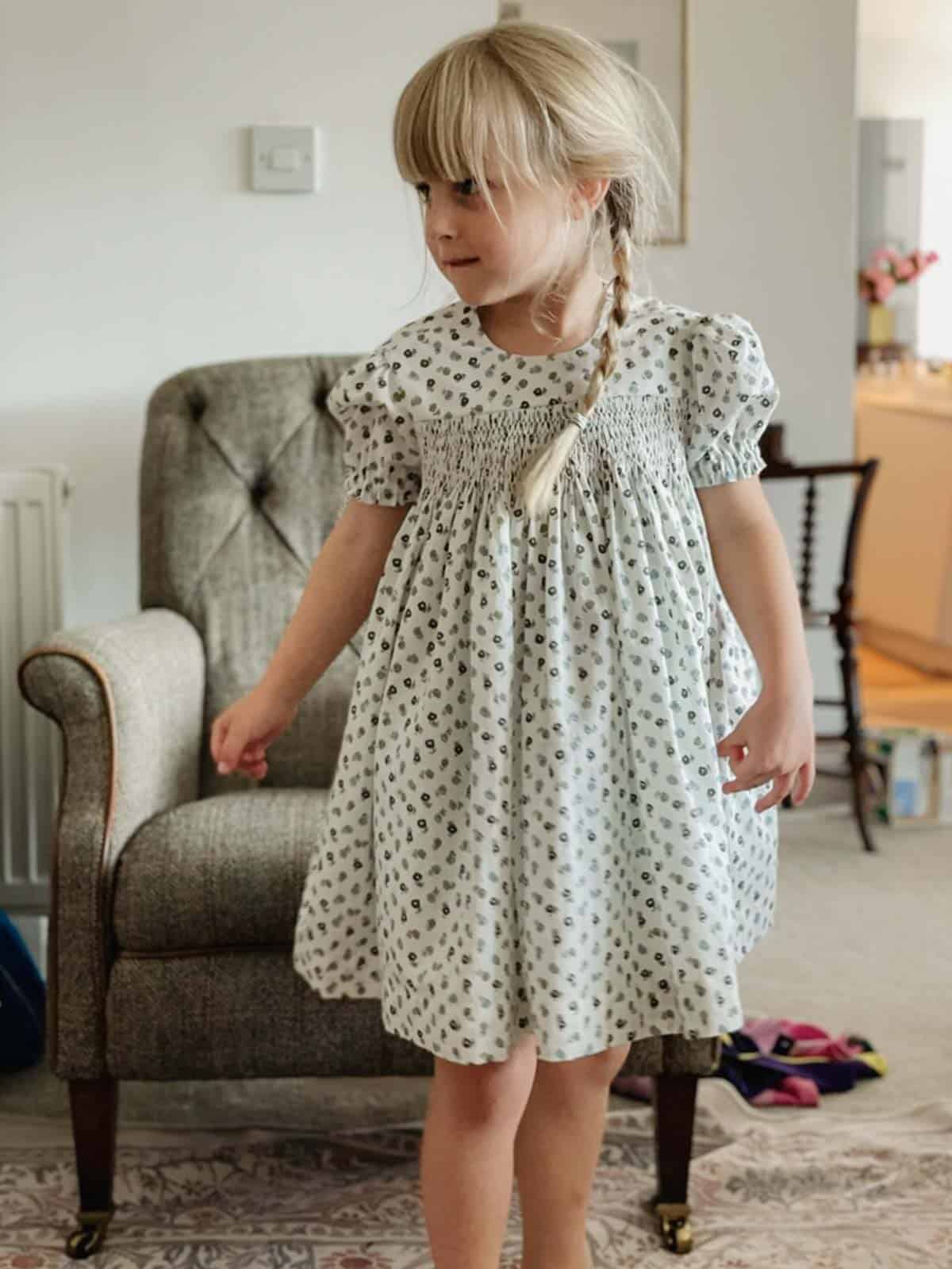A little girl wears a handmade smocked dress with blue and green florals