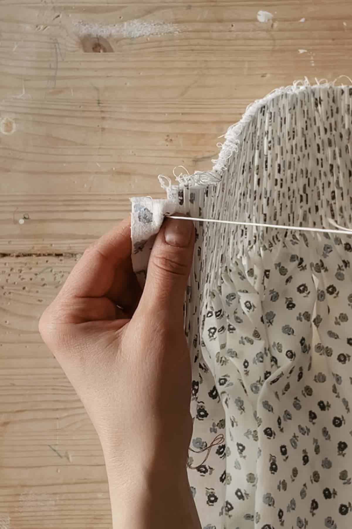 A person brings a needle and thread up between the first and second pleats
