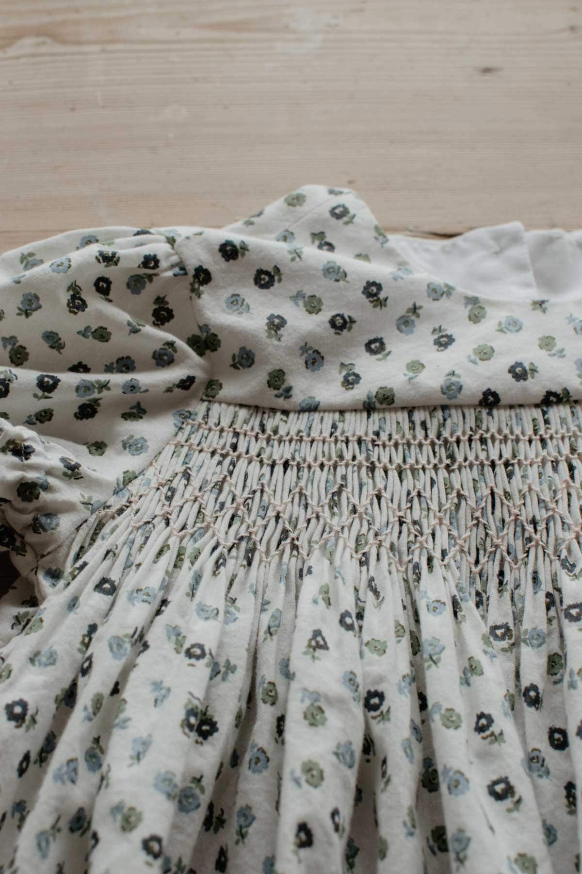 A close up of smocking stitches - cable stitch and trellis stitch - in pink thread on a floral fabric