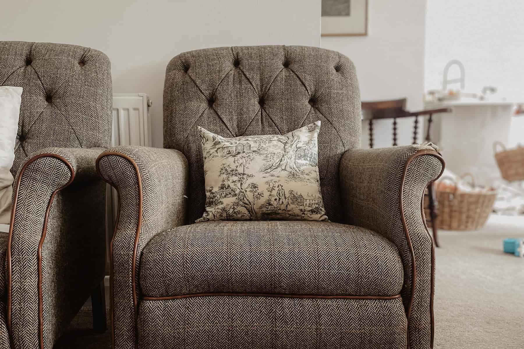 A toile fabric pillow cover sits on a harris tweed armchair