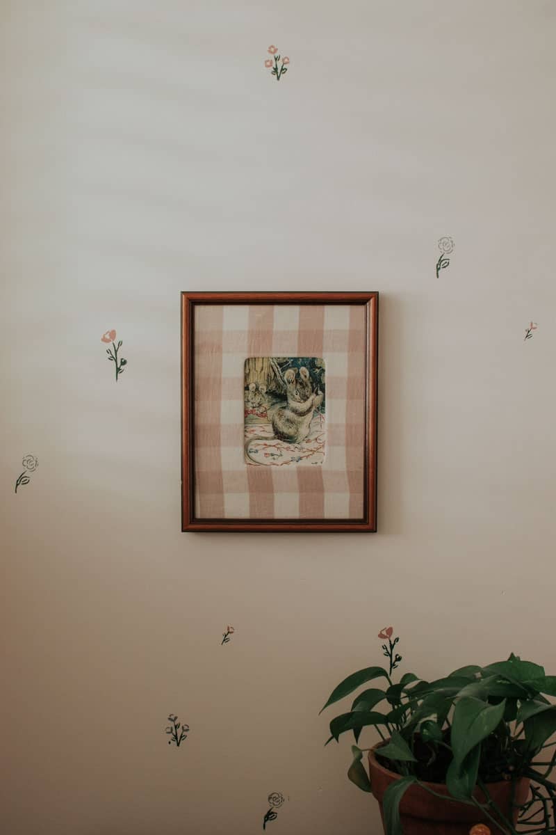 A picture of a mouse on a wall covered with stencilled flowers