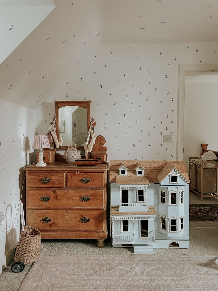 A wall with stencil flowers behind an antique dresser and dollhouse