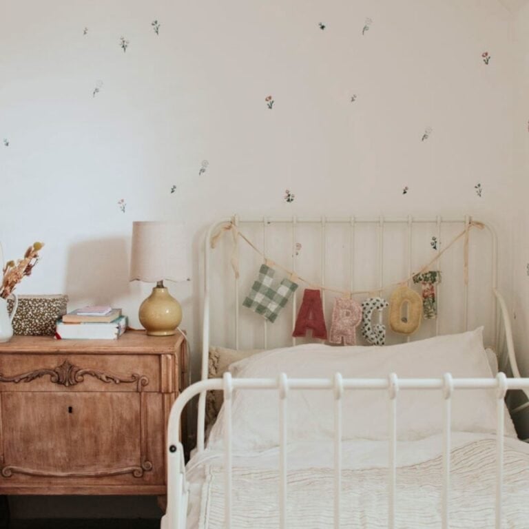 Soft pastel bedroom with floral wall stencils and vintage wooden sideboard, highlighting cosy, shabby chic interior design.