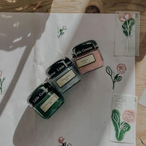 Small jars of Little Greene paint in green, pink, and grey on wooden surface, ideal for interior décor projects.