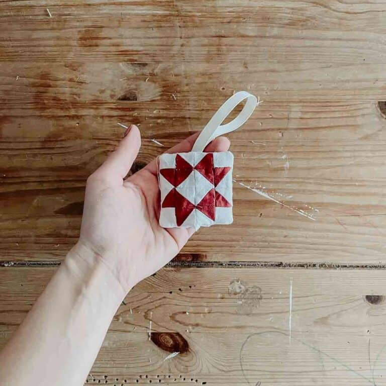 A hand holds a mini Christmas patchwork decoration in front of a wooden table
