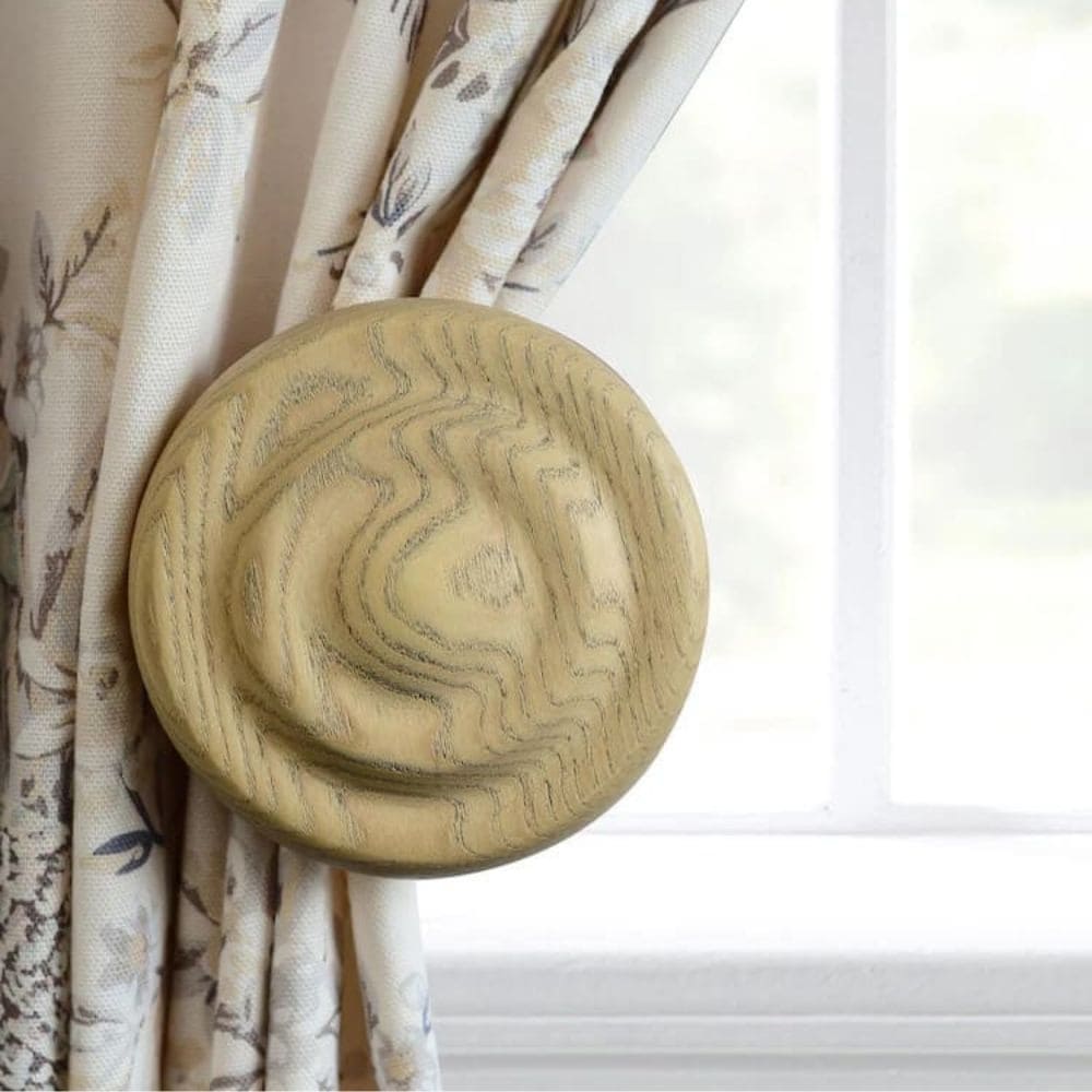 A round wooden curtain tieback secures patterned cream-coloured curtains next to a white-framed window, adding a cosy touch that can inspire ideas on how to make a bed canopy. The tieback’s natural wood grain finish suits any style.