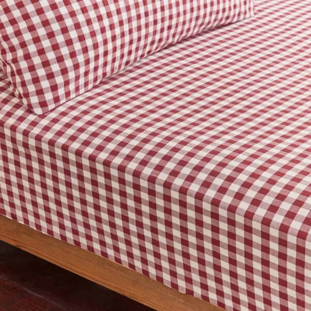 A close-up view of a bed with a red and white checked sheet and matching pillowcase on a wooden bed frame, offering cosy inspiration for how to make a bed canopy in your own bedroom.