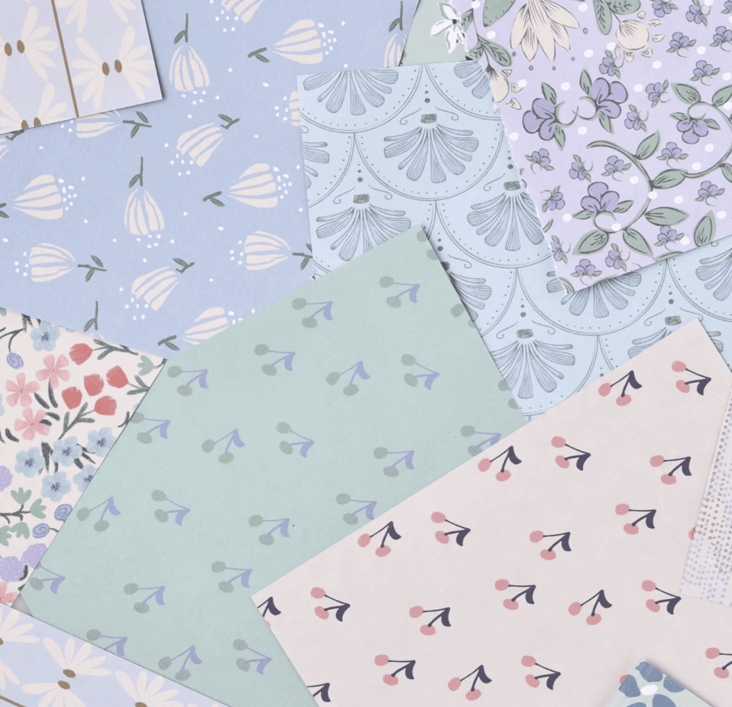 Sheets of pastel-coloured miniature paper with various floral and botanical patterns, perfect for affordable DIY dolls’ house wallpaper, are arranged in an overlapping, decorative manner.