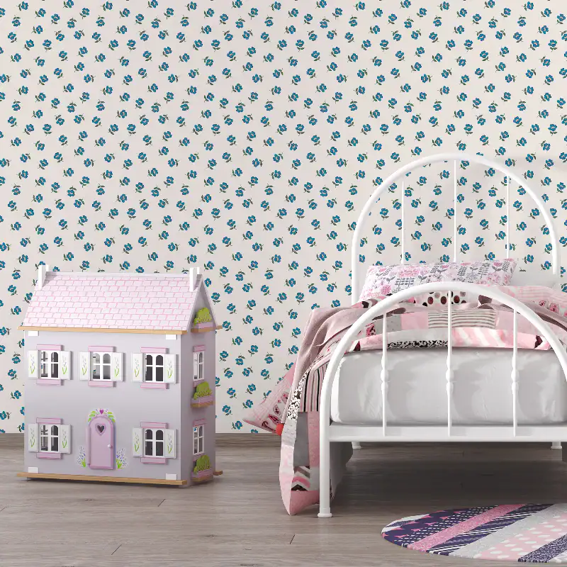 A white metal bed with pink and white bedding sits next to a pastel-coloured doll's house featuring DIY doll's house wallpaper, against a wall with blue floral patterned wallpaper. A round striped rug is partially visible on the floor.