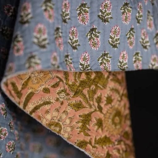 A close-up of fabric with a blue side featuring pink and green floral patterns, alongside fabric eggs, and a folded-over edge revealing the underside with a brownish design of yellow and green flowers and leaves.