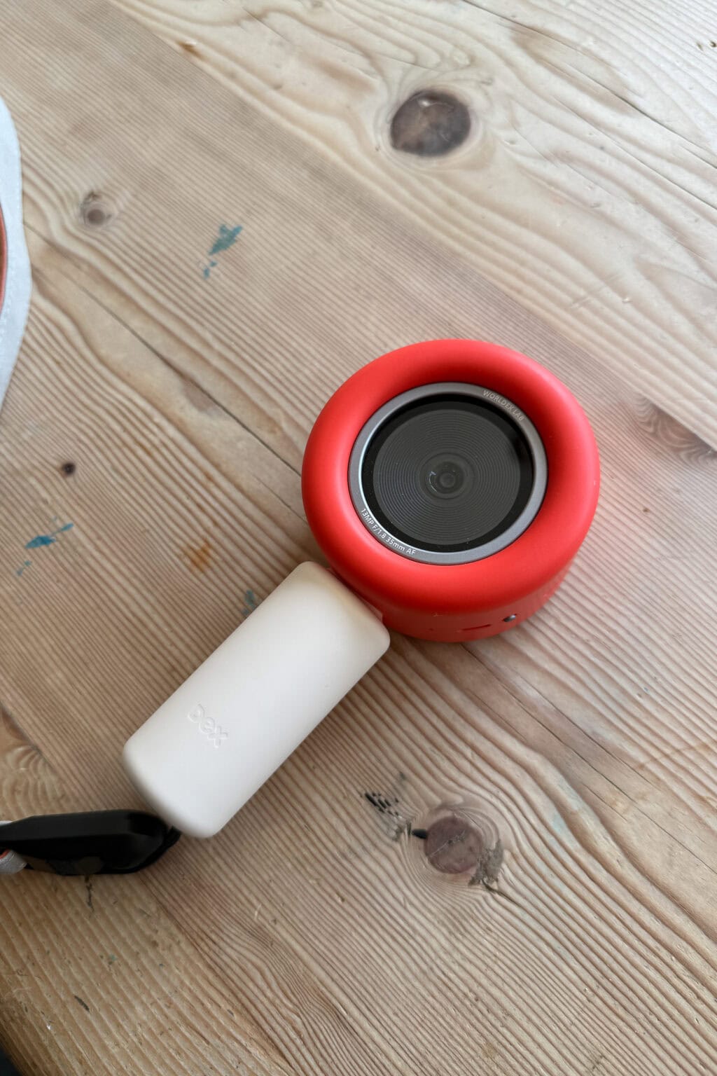 A dex camera with a black centre sits on a light wooden surface.