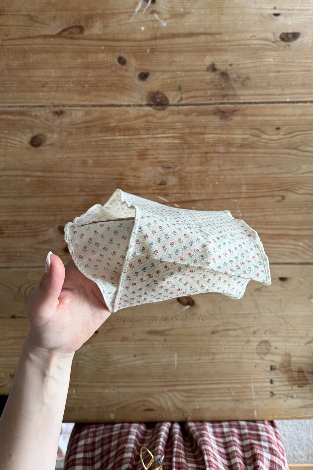 A hand holds up two pieces of floral fabric The person is wearing a red and white checked garment.