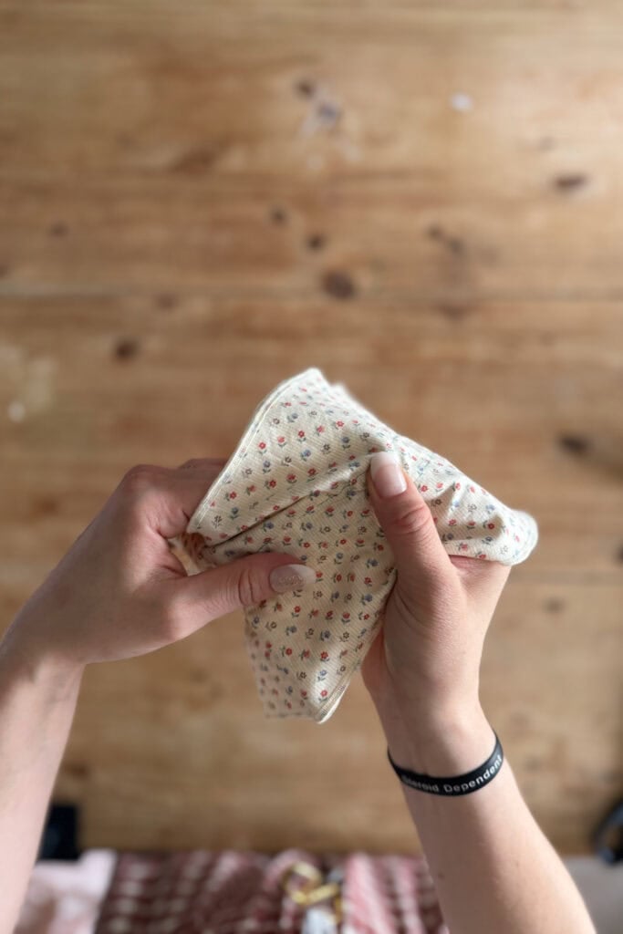 A person holds and folds a small, cream-coloured cloth with a tiny red and green floral pattern